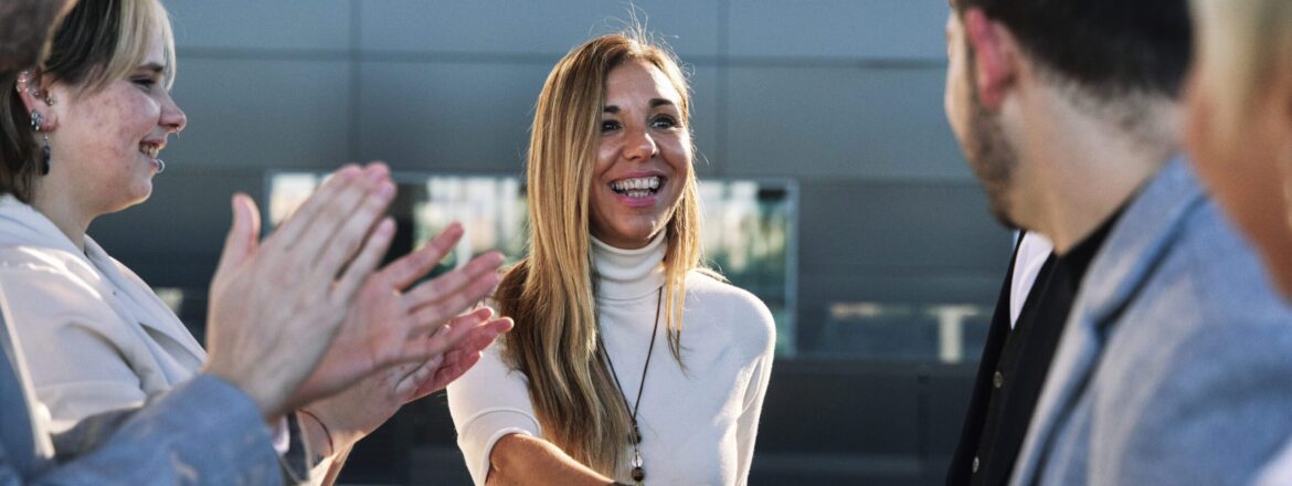 group of business people applauding and showing their appreciation to a successful businesswoman who, with a radiant smile, shakes hands with one of them